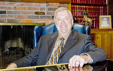 Hiring an Attorney May Help Reduce the Stress of a Divorce 7 Smiling man in pinstripe suit and gold tie seated in blue leather chair near brick fireplace with law books on shelves beh...