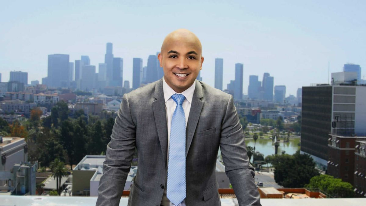 Lem Garcia Law Marks a Milestone of Serving Over 1000 Personal Injury Clients with a Client-Centric Approach 3 Smiling bald man in gray suit and light blue tie posing with Los Angeles skyline and park in background