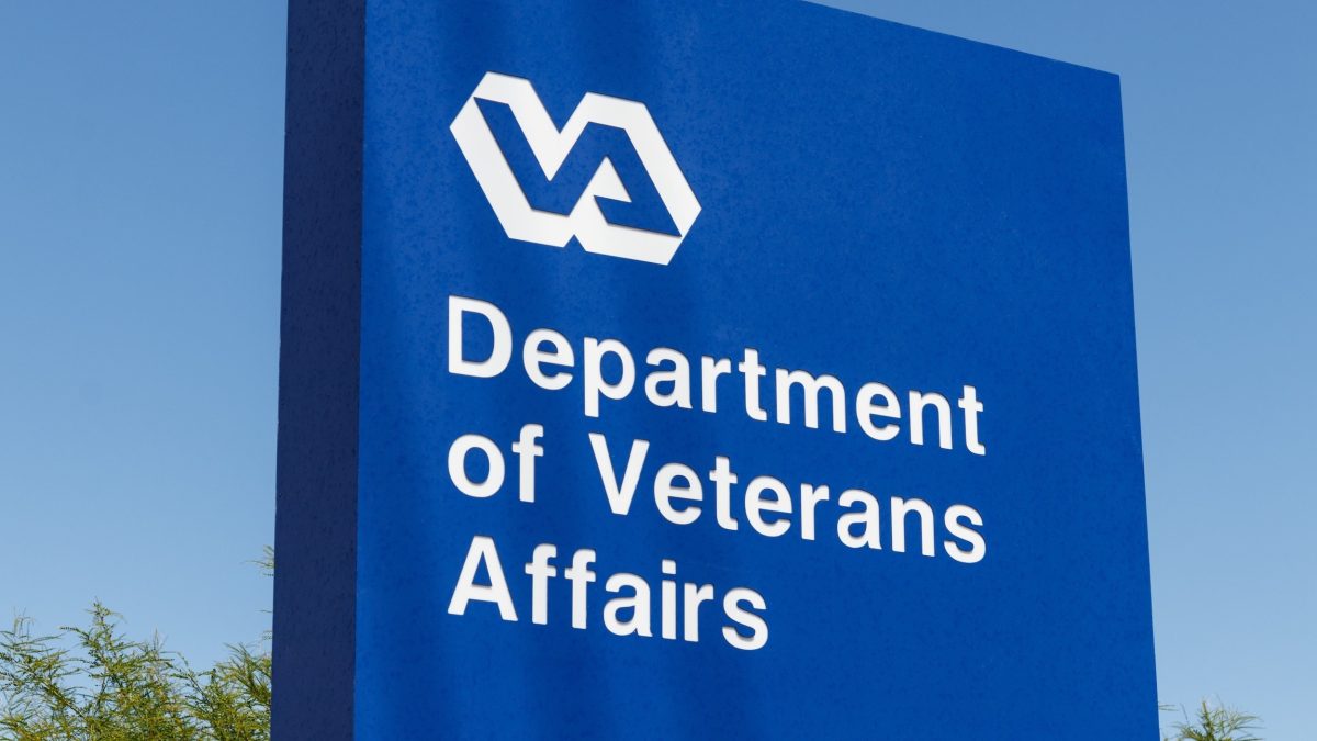 Blue outdoor sign with white VA logo and text reading Department of Veterans Affairs against a clear blue sky