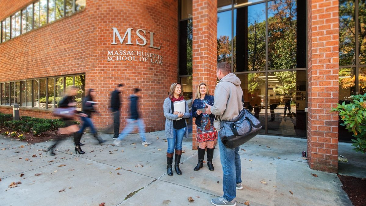 Three students conversing outside the Massachusetts School of Law brick building with MSL signage on an autumn day.